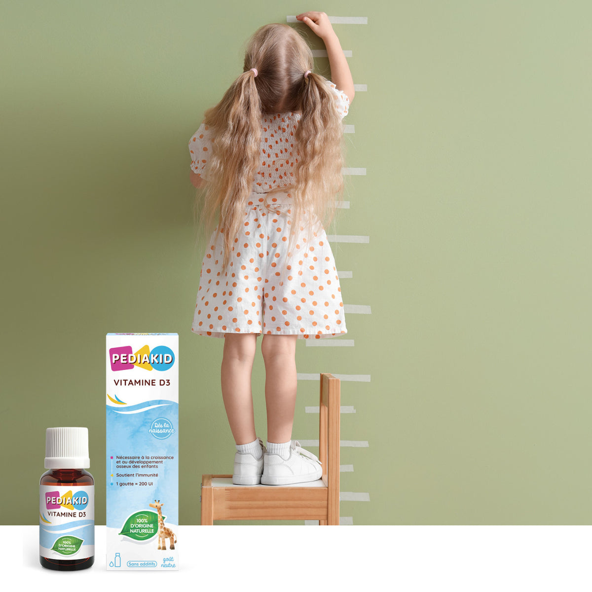PEDIAKID Vitamina D3 picături - fetiță care își măsoară înălțimea lângă perete, alături de flaconul cu picături